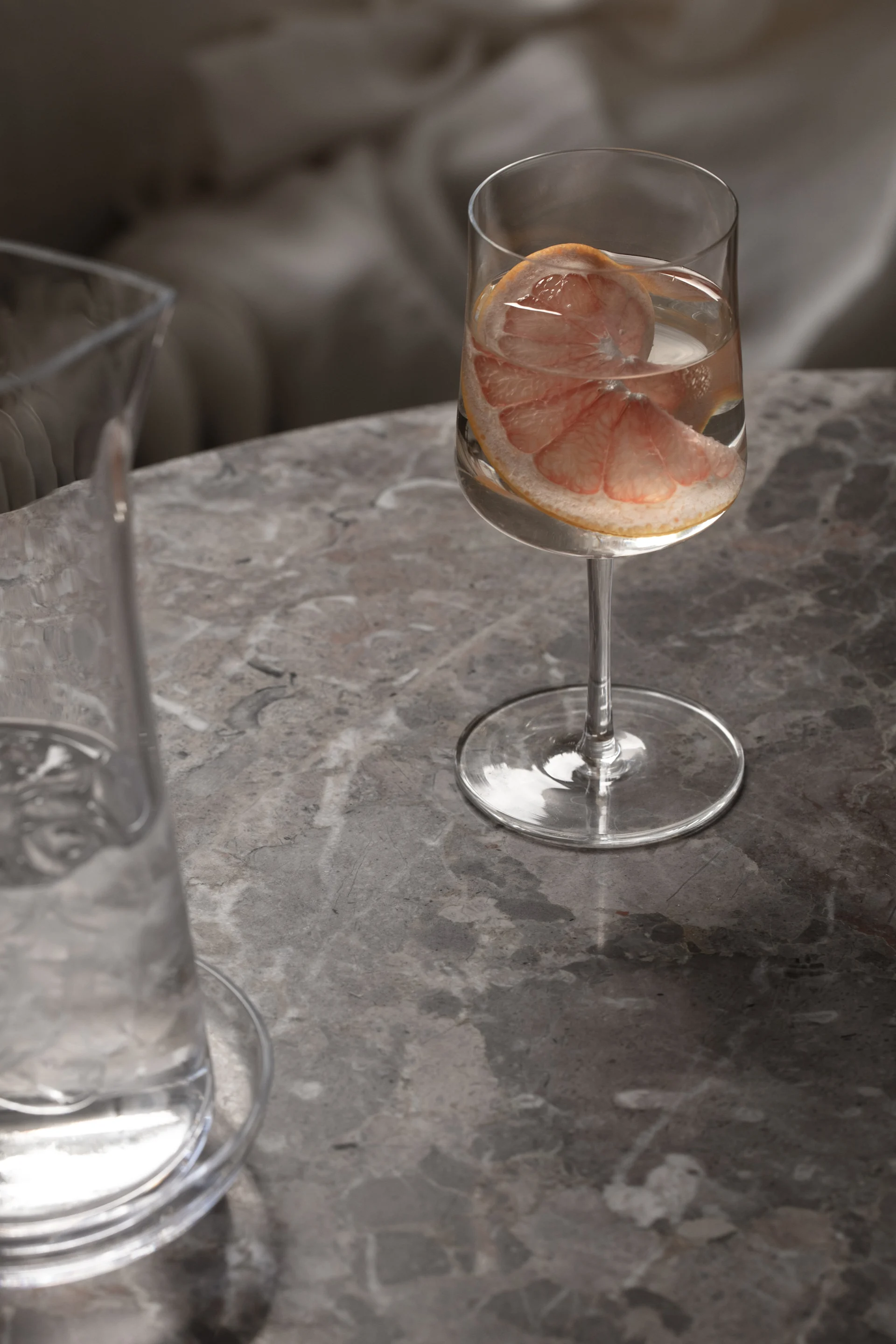A glass of water with grapefruit on a grey marble table, with a water carafe partially visible.