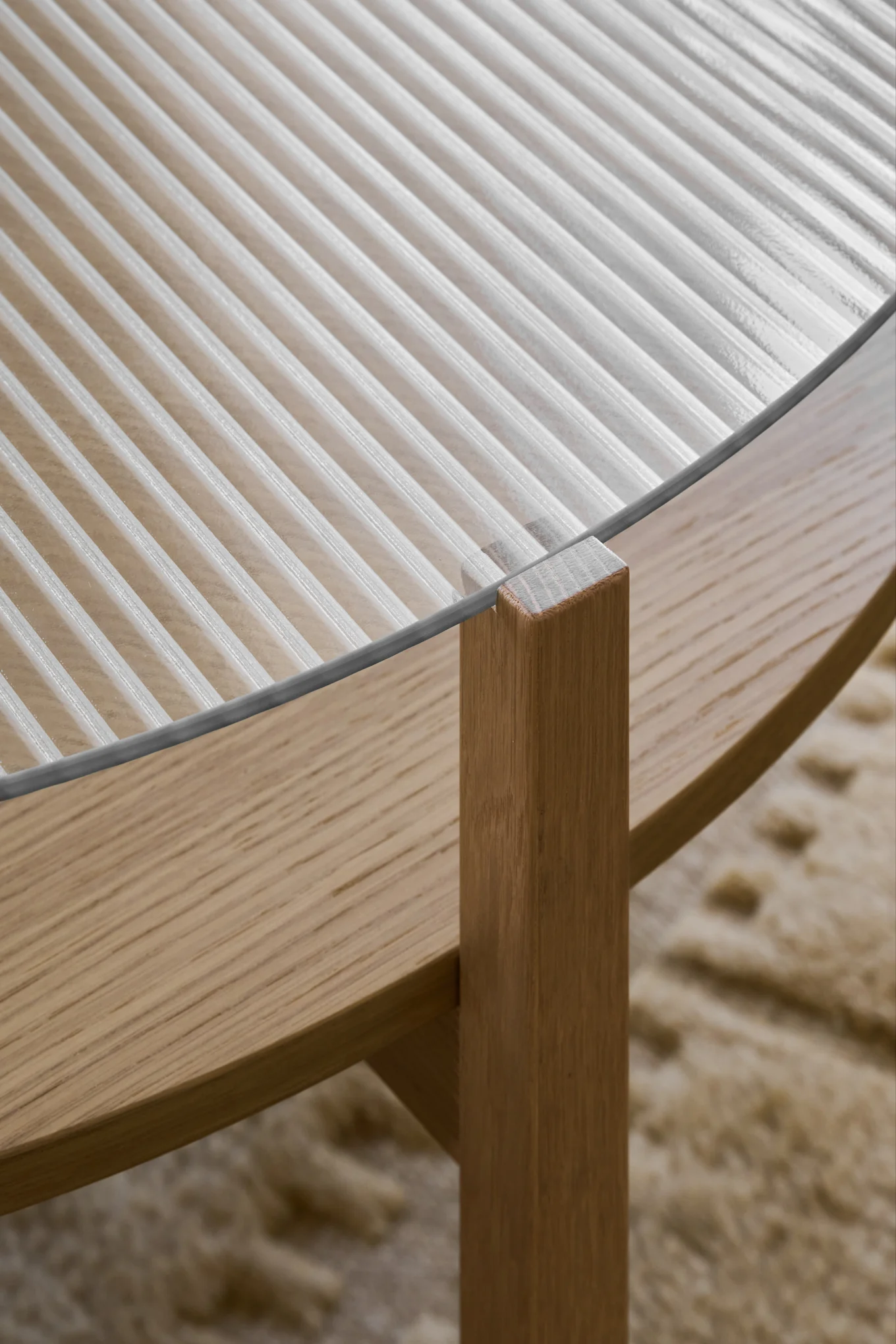 Close-up of a coffee table with a fluted glass top and light wood base.