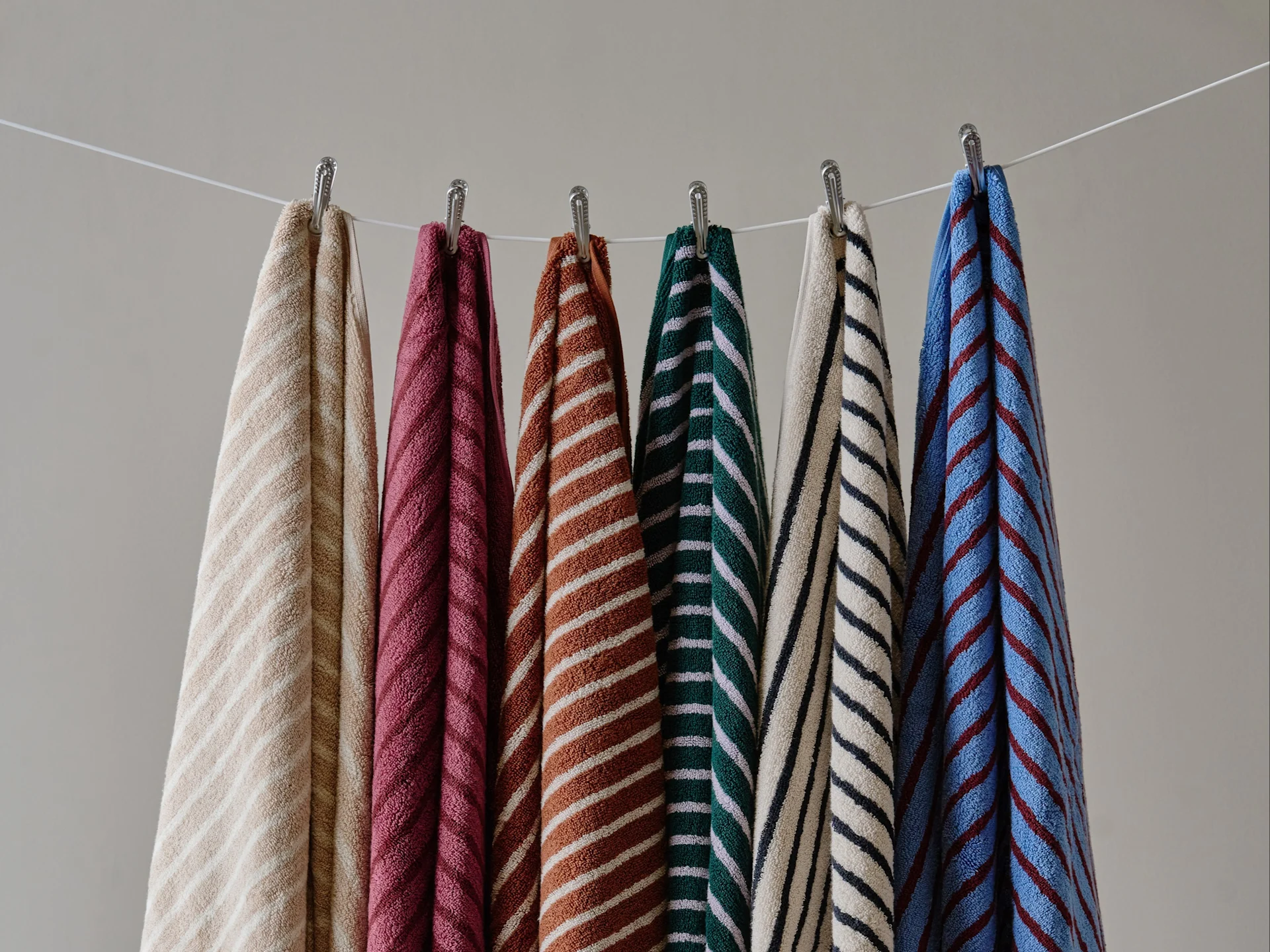 Six colorful striped towels hanging on a clothesline against a plain wall.