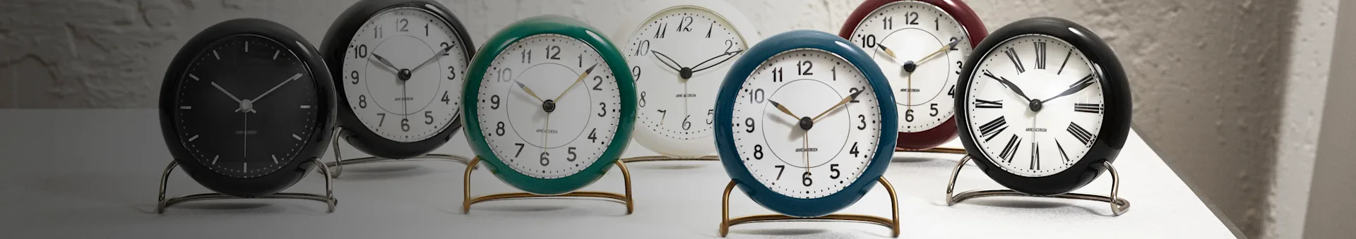 Seven vintage-style desk clocks in black, white, green, blue, and red, featuring Arabic, Roman, and minimalist dials.