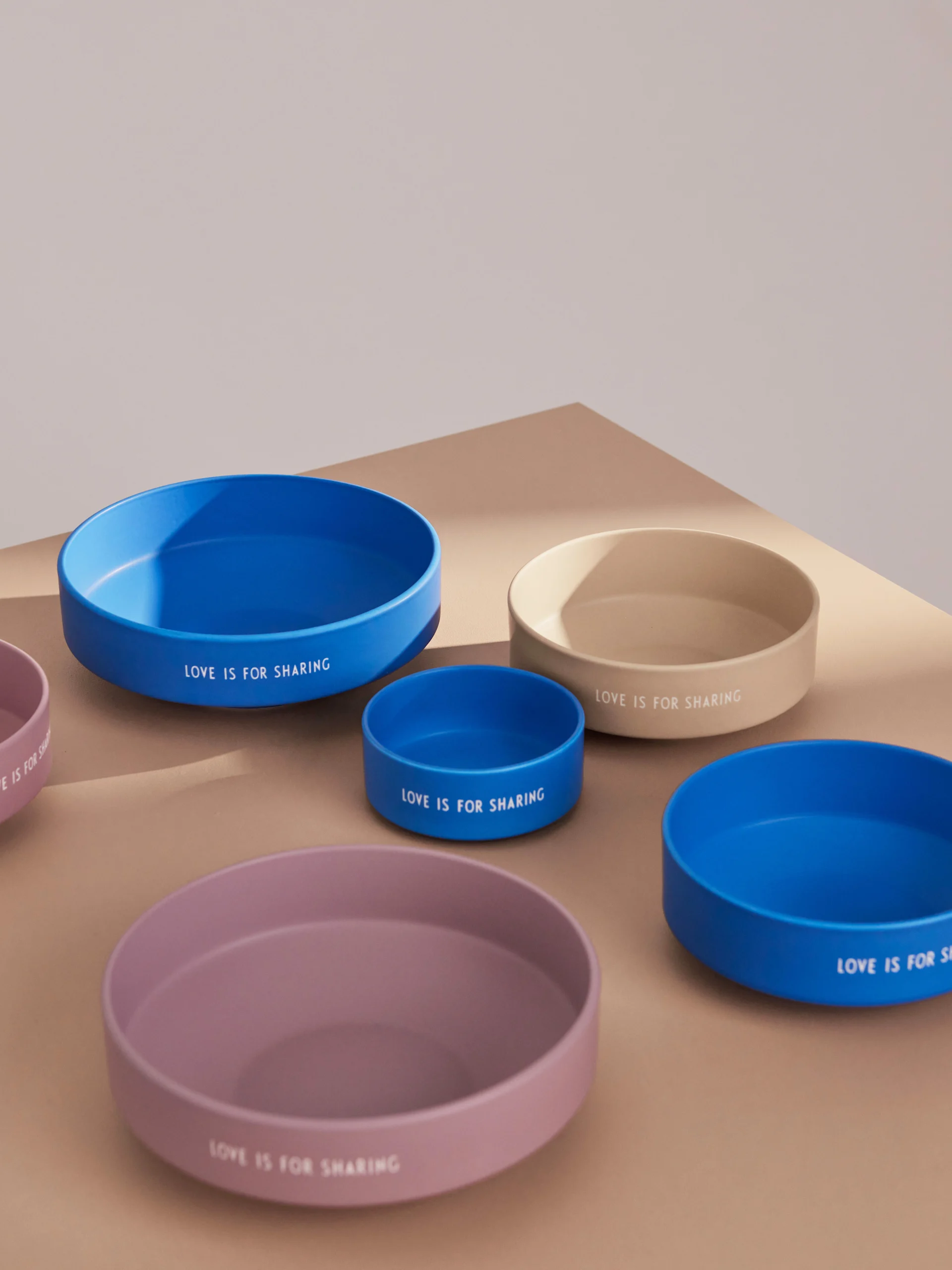 Assortment of round bowls in blue, beige, and purple, each inscribed with 'LOVE IS FOR SHARING'.