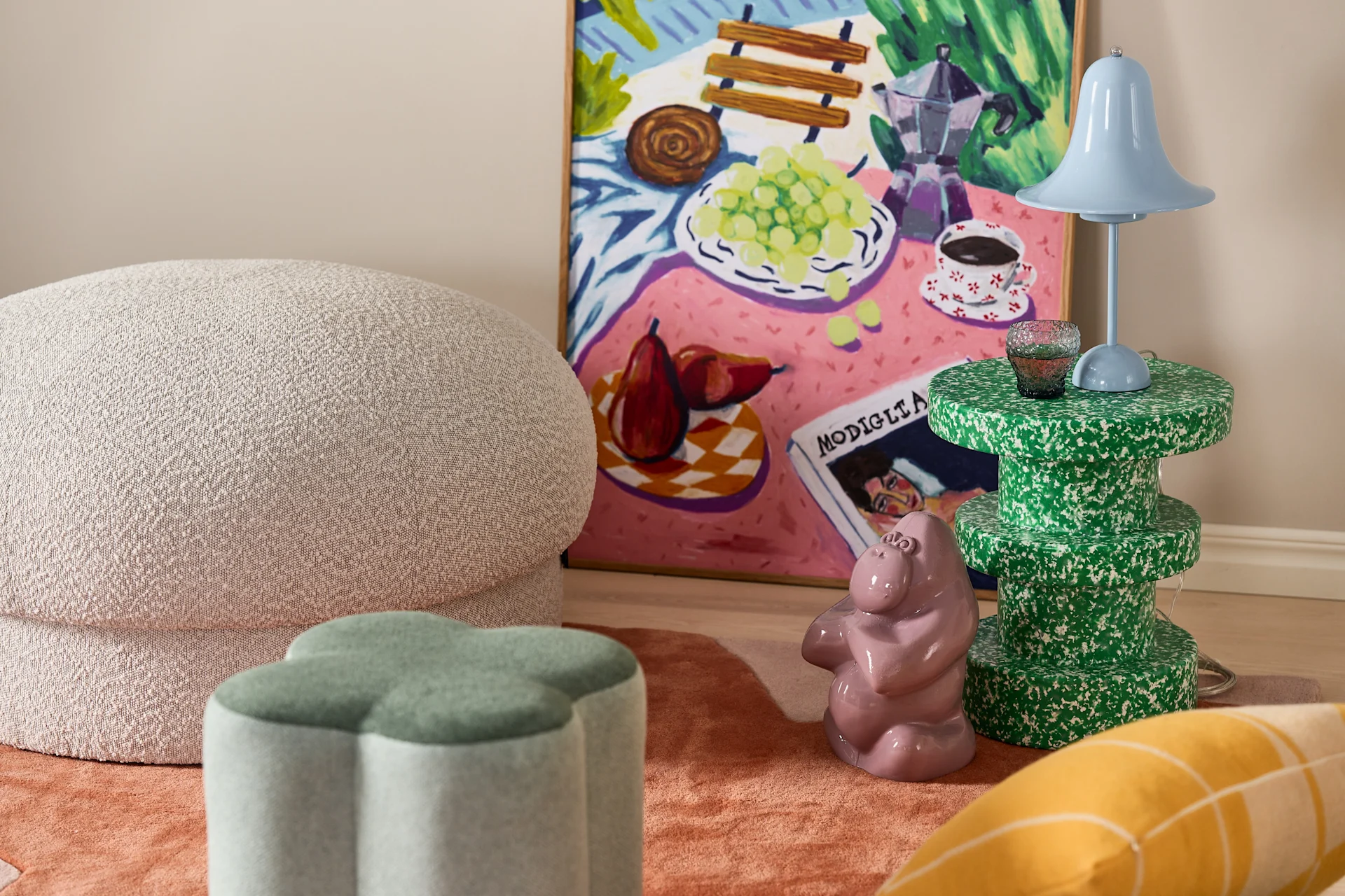 Eclectic room decor: textured ottoman, green clover stool, blue lamp, speckled green table, pink hippo, and colorful painting.