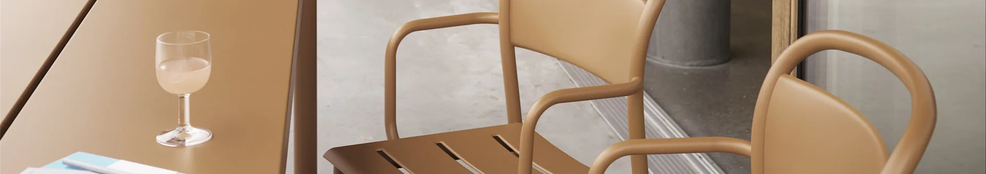 A champagne flute on a brown table with two matching brown chairs featuring curved armrests.