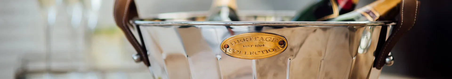 Silver ice bucket with a brown leather handle and a brass 'Heritage Collection' plaque.