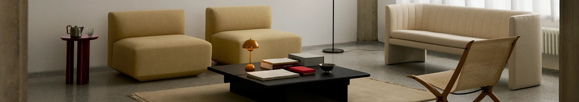 A modern living room with two mustard armless chairs, a black coffee table, a cream ribbed sofa, and a woven wooden chair.