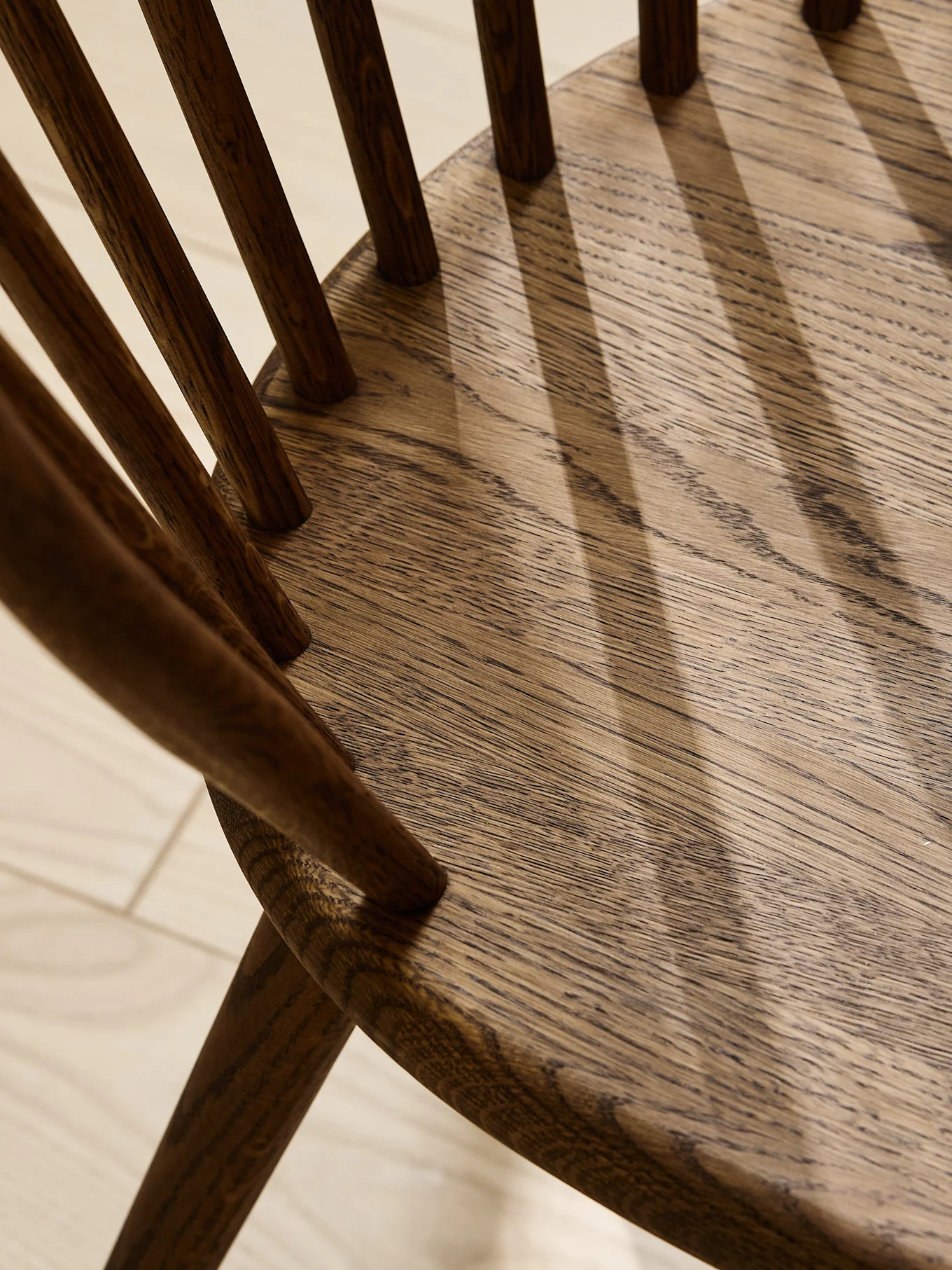 Close-up of a dark oak wooden chair seat and back spindles, showing natural grain and shadows.