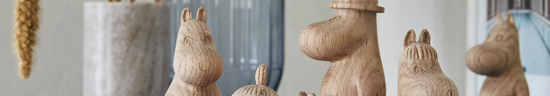 Several carved wooden Moomin-like figures of varying sizes, showcasing natural wood grain, arranged in a line.