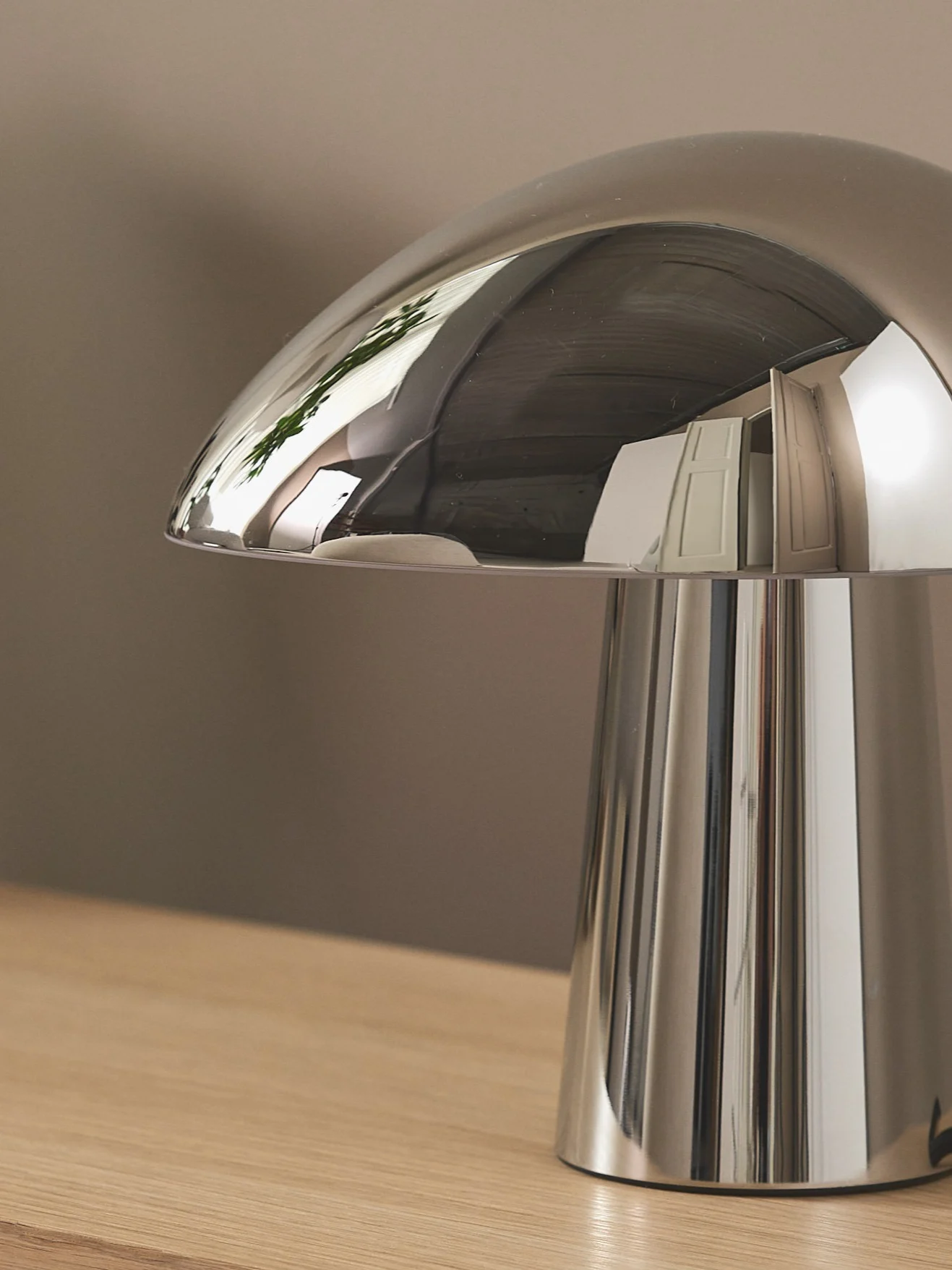 Chrome mushroom lamp on a wooden table, reflecting a room interior.