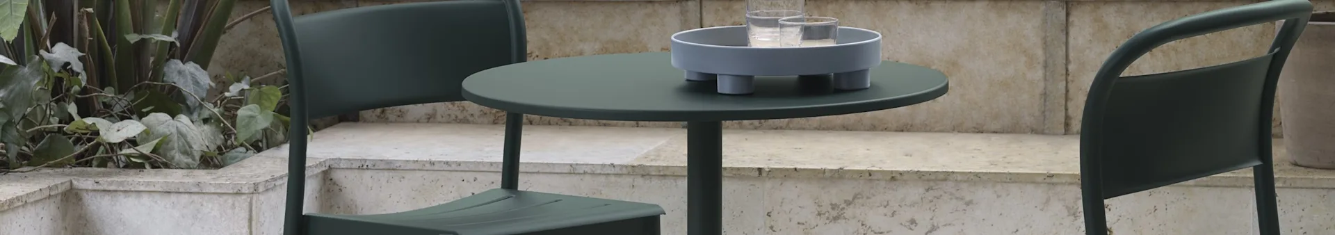 Two dark green outdoor chairs and a round table with a light grey tray and two water glasses.