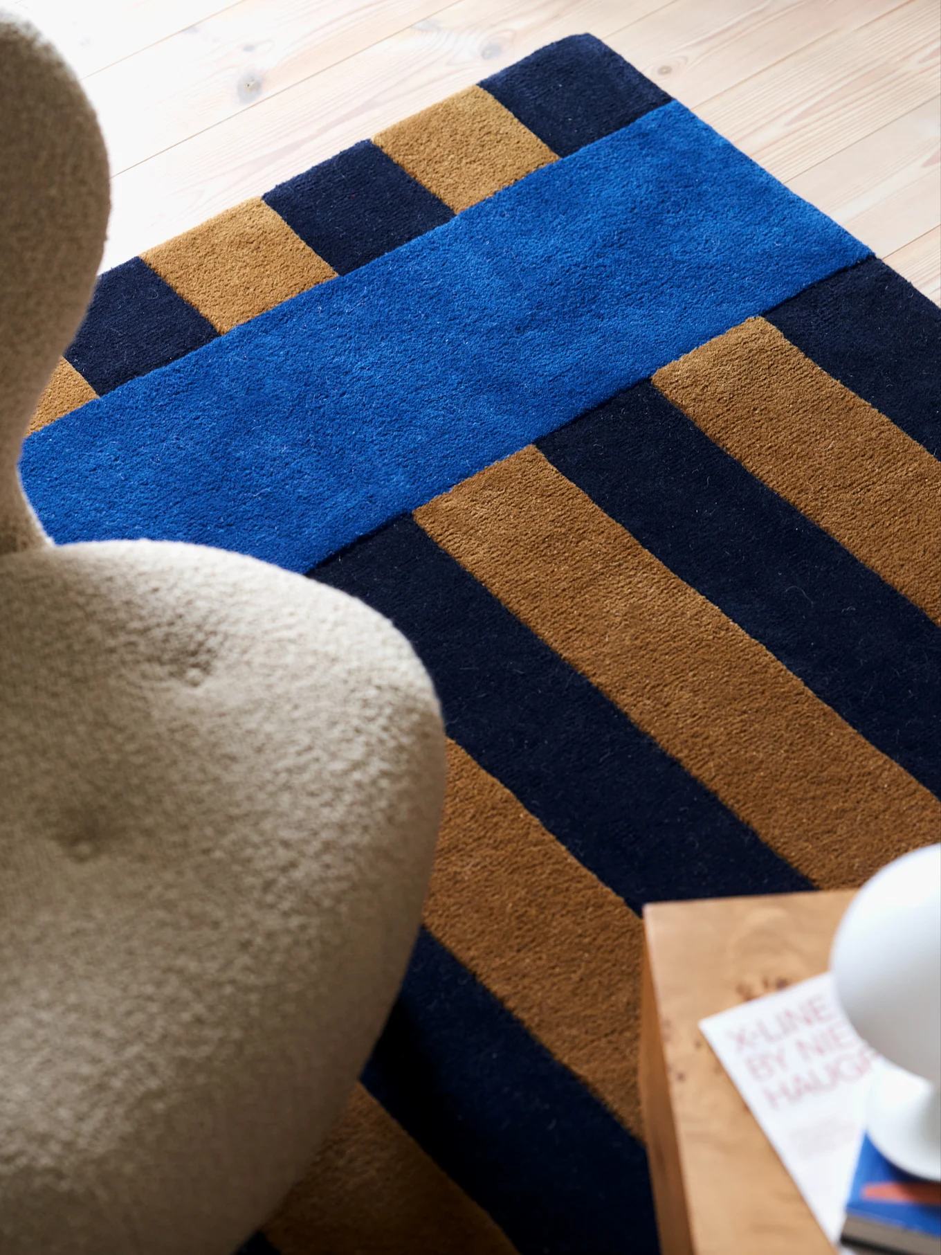 Modern rug with diagonal dark blue and tan stripes, and a bright blue horizontal stripe, on a light wooden floor.