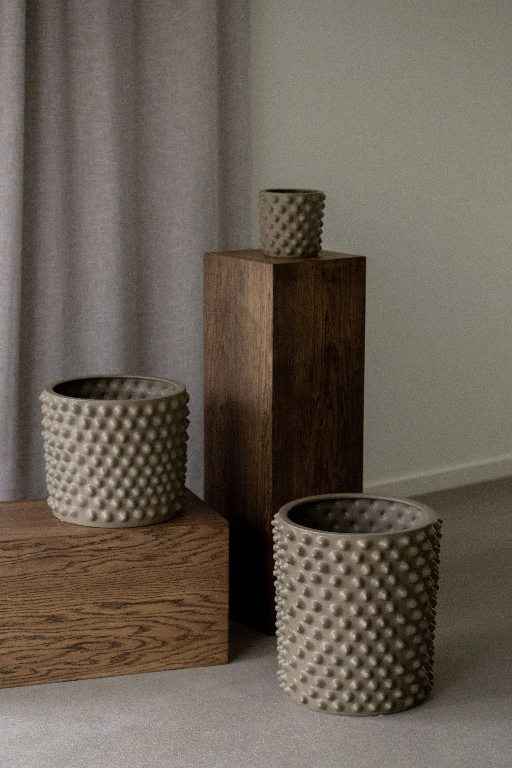 Three beige textured planters on dark wooden pedestals.