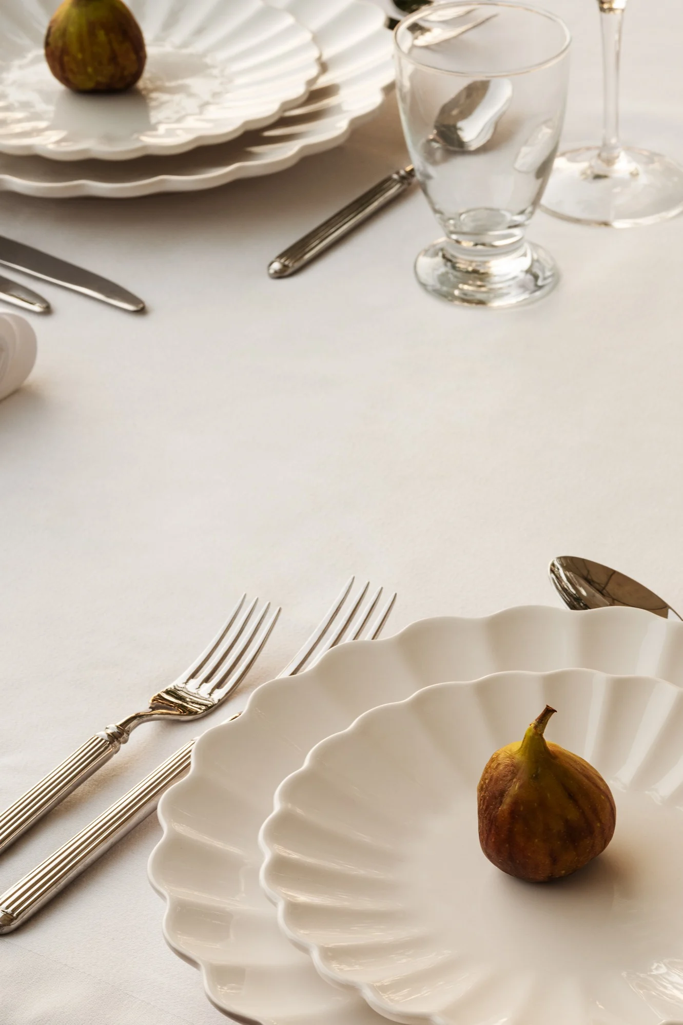 Elegant table setting with white ruffled plates, silverware, and a fig on each plate.