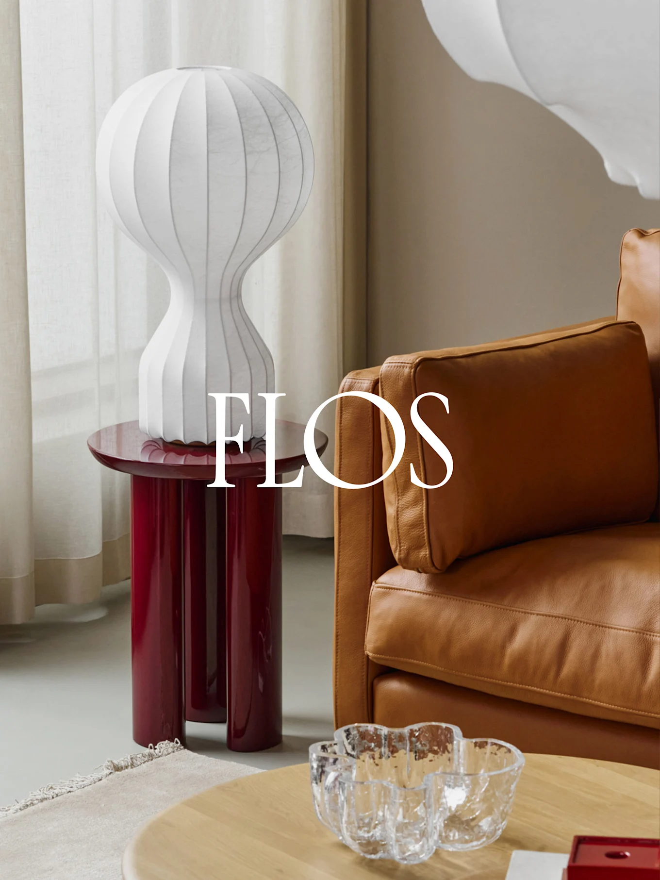 White ribbed table lamp on a glossy red side table next to a tan leather sofa.