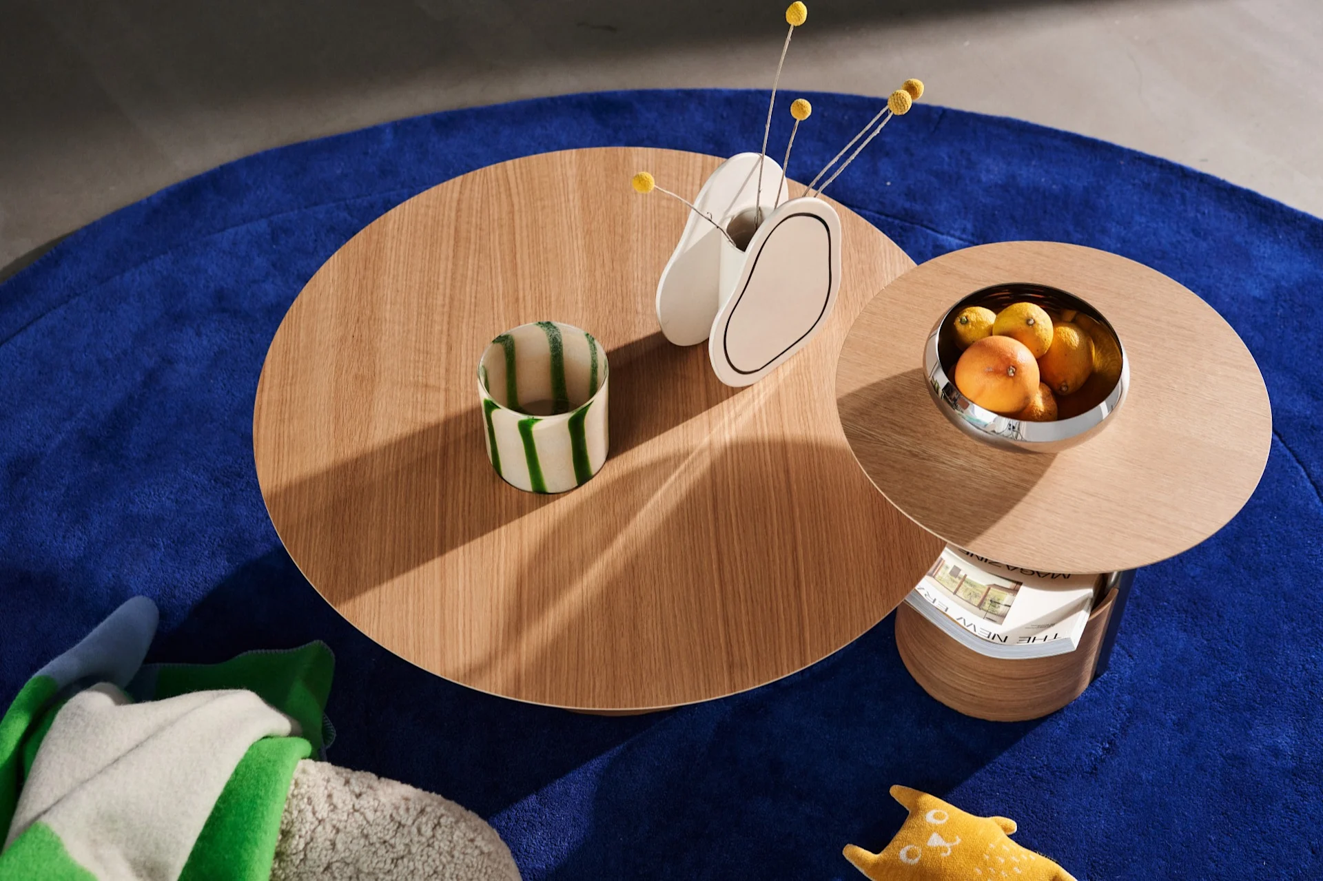 The Parasol tables from above on a blue rug with a vase and a bowl of oranges and lemons.
