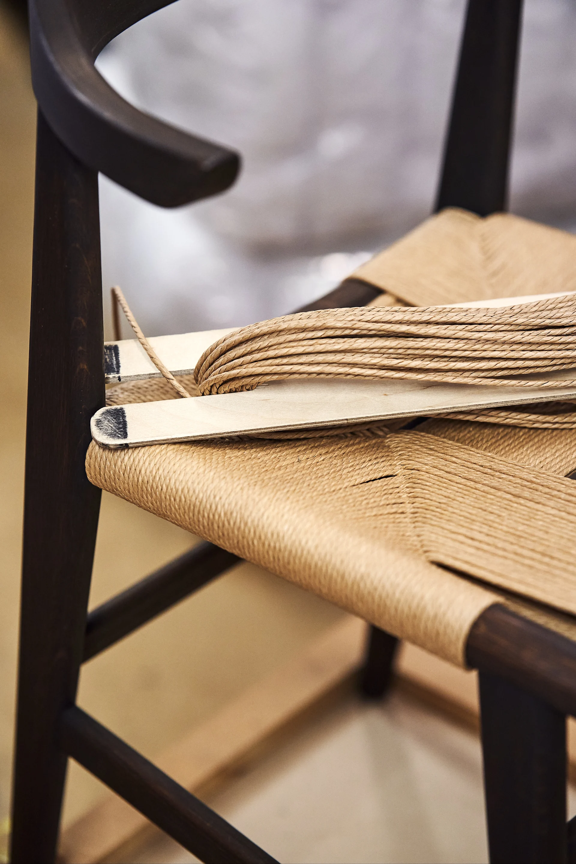 Close-up of a dark wooden chair with a woven paper cord seat and coiled cord on top.