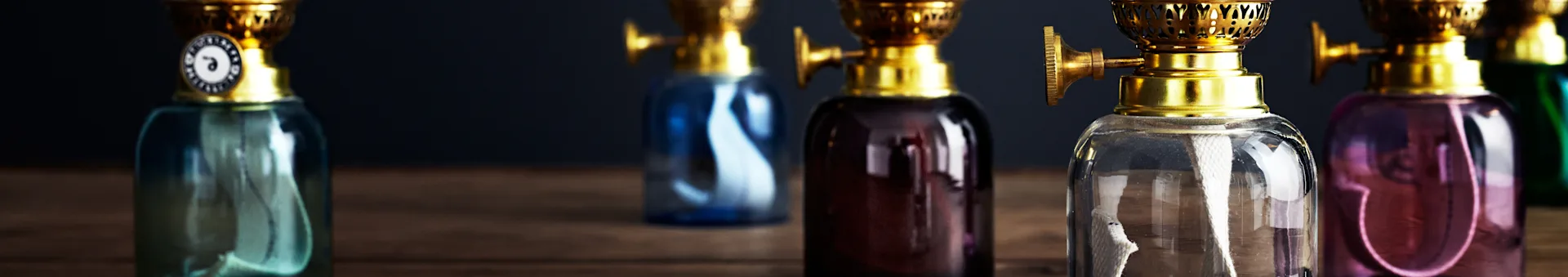 A row of colorful vintage oil lamps with brass tops on a wooden surface.