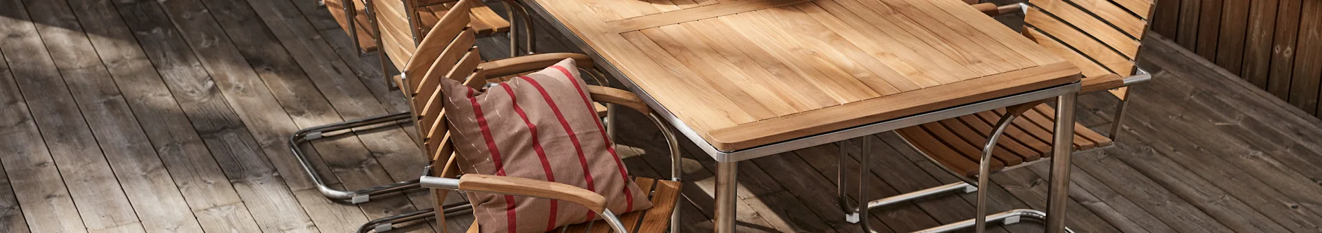 Slatted wood outdoor dining set with metal frames on a wooden deck. A striped cushion rests on one chair.