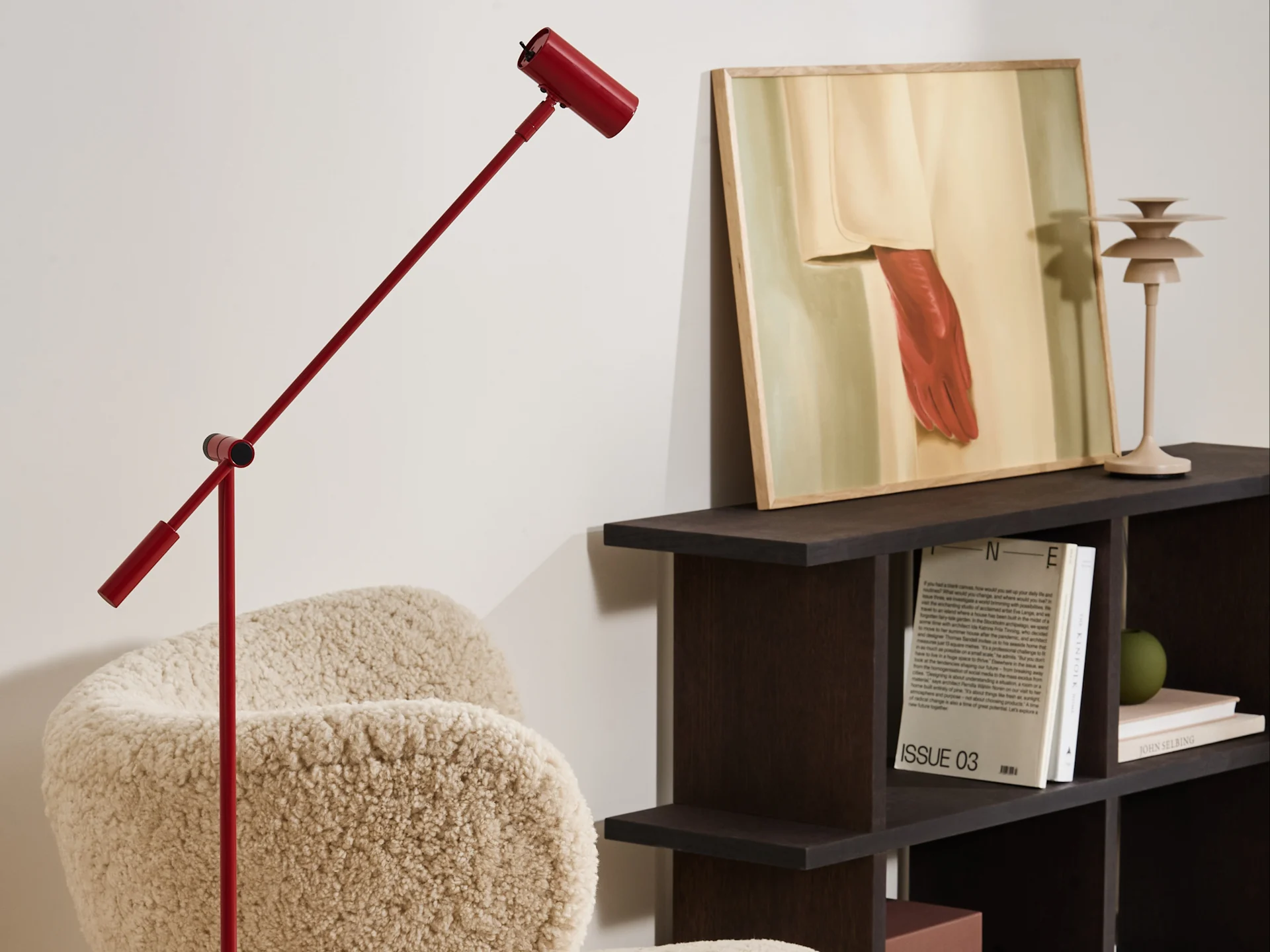 A modern living room with a red floor lamp, a cream bouclé armchair, and a dark wood shelf displaying art and books.