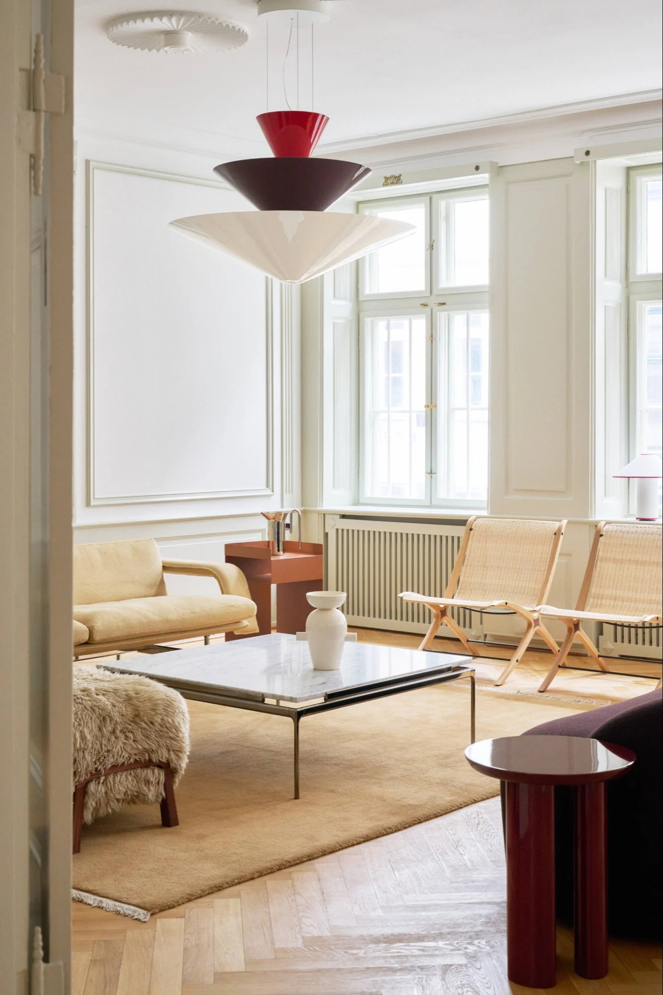 A contemporary living room with a tiered pendant lamp, light yellow sofa, cane chairs, and marble coffee table.