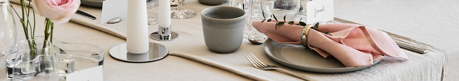 Elegant table setting with linen, a grey plate, pink napkin, white candle, a rose, and a name card for Sarah.